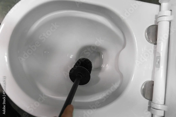 Obraz Hand holding a black toilet brush, scrubbing a white ceramic toilet bowl, promoting cleanliness and hygiene while tackling dirt and grime in the bathroom environment