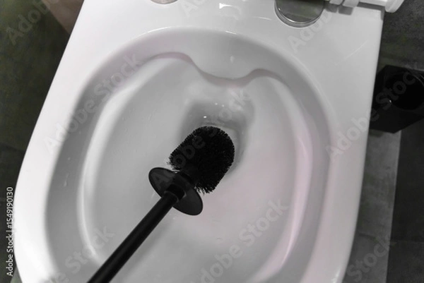 Obraz Modern black toilet brush hovering over an open white toilet bowl, preparing for cleaning in a contemporary bathroom featuring a stylish gray tiled floor