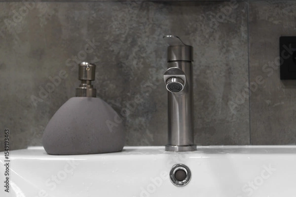 Obraz Featuring a sleek, modern faucet and stylish soap dispenser atop a clean white sink, enhancing the minimalist aesthetic against a textured gray tiled wall