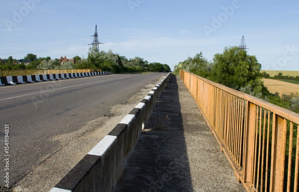 Fototapeta A road with a fence and trees