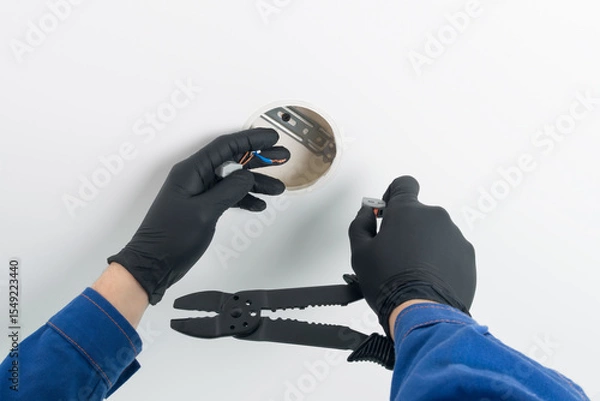 Fototapeta hands of a master in uniform in protective black gloves and with a tool, repairing electrical wiring lighting of a suspended ceiling