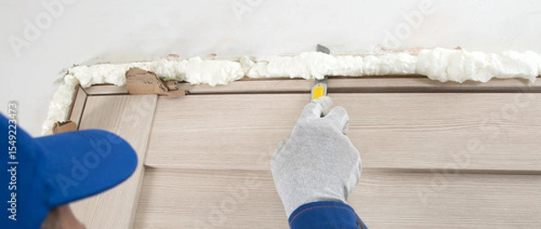 Fototapeta close-up, master in protective gloves and uniform, cuts the mounting foam of the doorway, after installation
