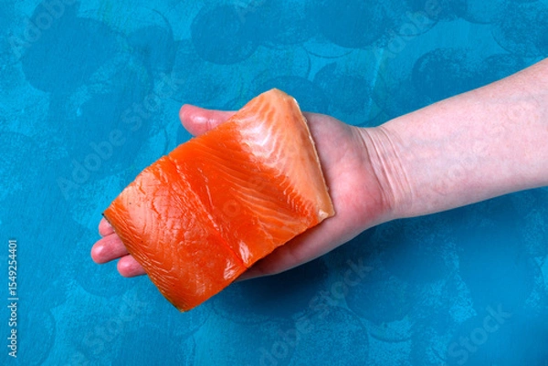 Fototapeta Trout fillet piece in hand on turquoise wooden board. Fresh sea ingredient. Product selection, quality determination. Top view