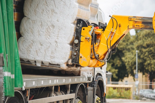 Obraz Telehandler forklift unloads large rolls of rockwool insulations from delivery truck at construction site