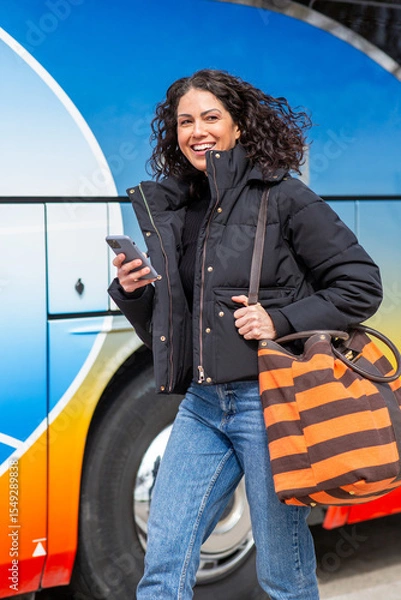 Obraz Smiling travel woman walking with bag and cellphone by bus