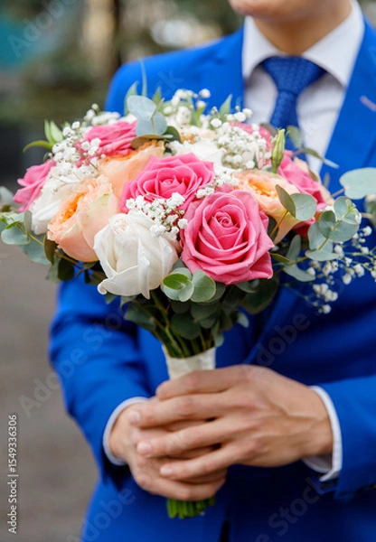 Obraz Groom in a blue suit holding a wedding bouquet. Close-up of hands and floral arrangement, no face visible. Elegant composition with focus on romantic detail and emotional symbolism.