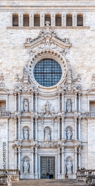 Fototapeta Close-up of Girona Cathedral’s ornate Baroque facade with intricate stone carvings, statues, and a rose window, Spain. Features sacred sculptures, decorative details, and 1733 date inscription