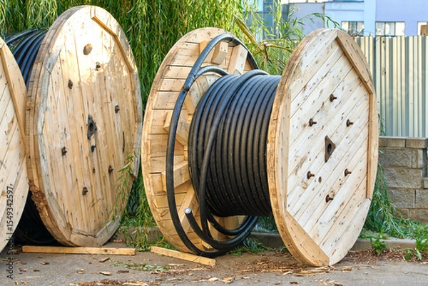 Fototapeta Coiled wire stored on large round wooden spools prepared for electric or telecom network deployment wiring work. Wooden cable drums organized and waiting for use in laying underground cables