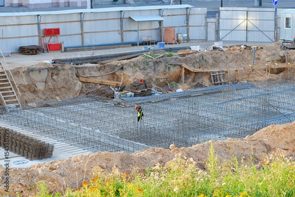 Fototapeta Construction site, steel rebar framework installed within an excavated trench for future concrete foundation in urban development. Foundation work, building site with steel rebar grid, excavation pit