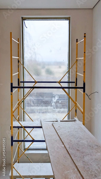Obraz Renovation scene showing a flight of stairs beside a large, dusty window with scaffolding installed for construction work. The space is unfinished, highlighting ongoing interior remodeling efforts.
