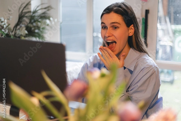 Fototapeta Woman smiles, young hipster working on a laptop at home, writing a message to friends, win in lottery, have a good news, make win gesture and screaming. Happy business woman freelancer.