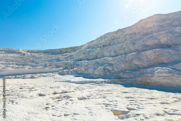 Obraz Natural calcium-rich travertine formations in Pamukkale, Türkiye, illuminated by bright sunlight. Unique white landscape formed by thermal spring waters flowing over terraced limestone surface