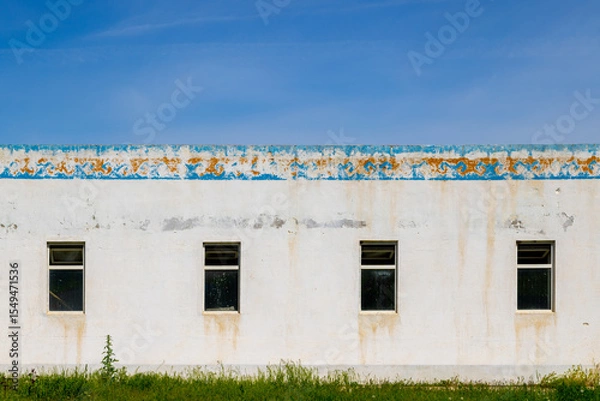 Obraz Weathered building with decayed Kyrgyzstani ornament and four windows in grassy area