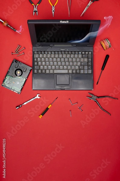 Fototapeta Old laptop surrounded by tools and electronic parts on red background. Concept of computer repair, vintage tech maintenance, and DIY electronics