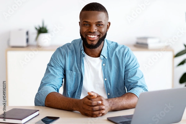 Fototapeta Portrait Of Young Black Freelancer Guy Sitting At Desk With Laptop Computer At Home Office, Looking At Camera, Smiling African American Entrepreneur Man Enjoying Remote Work And Self-Employment