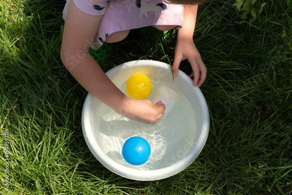 Fototapeta A child's hand reaches for the colorful balls floating in the water.