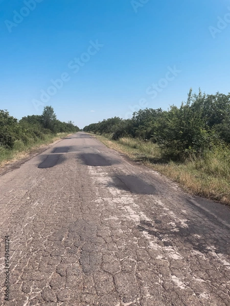 Obraz Cracked and patched road leading into overgrown wilderness. The concept of societal neglect, decay in rural development, and visual rawness.