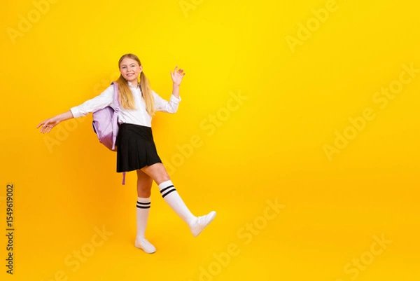 Obraz Happy student girl celebrating school success on bright yellow background with backpack and uniform skirt, joyful mood