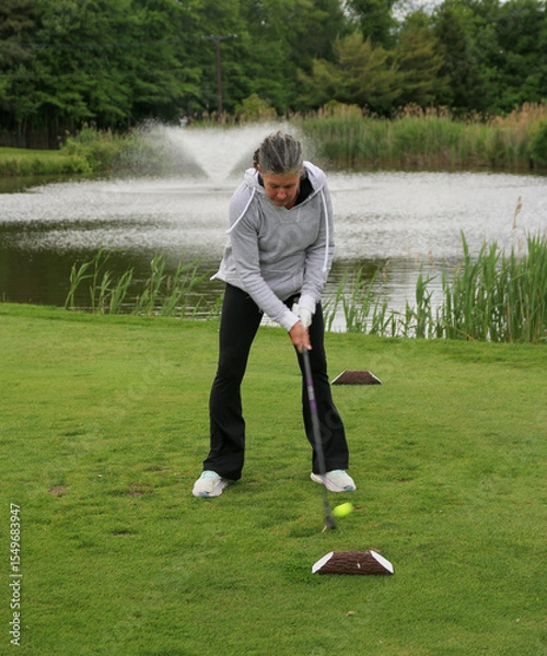 Obraz Woman Practicing Golf Swing on a Green Near a Peaceful Pond