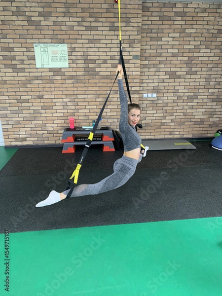 Obraz Young Woman in Grey Sportswear Doing Front Split on Tatami Mat in Gym