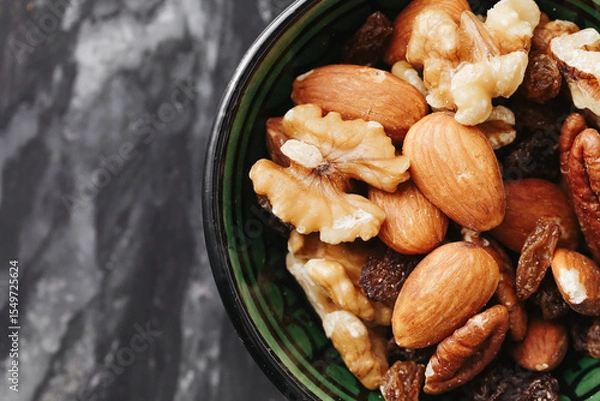 Fototapeta Mixed nuts in black bowl. Healthy snack with almonds and walnuts. Natural source of protein and fat. Fresh dry food on dark kitchen background. Diet and nutrition concept.