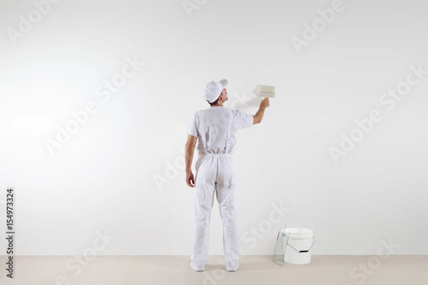 Fototapeta Rear view of painter man looking at blank wall, with paint brush and bucket, isolated on white room