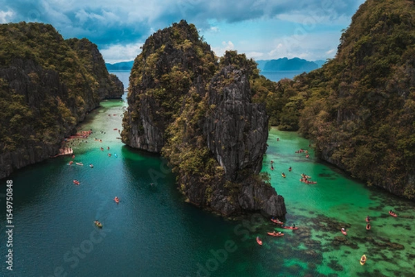 Obraz Tourists Kayaking Through the Turquoise Waters of Big Lagoon with impresive cliffs and bangka boats moored in a sunny day in Minoloc Island, El Nido, Palawan, Philippines