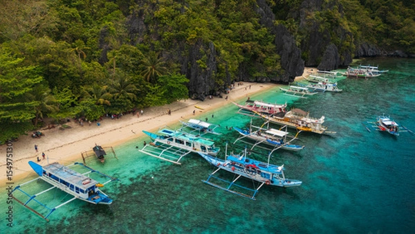Obraz Aereal view of Colorful Bangka Boats Docked on the Crystal-Clear Waters and Coral Reefs of Entalula Island with a beautiful beach with people in El Nido, Palawan, Philippines