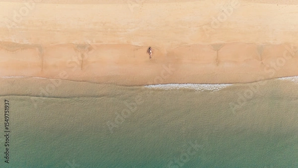 Obraz Bird's eye top aerial view of woman relaxing in sandy beach in the pristine turquoise shoreline and sweeping coastal landscape of Nacpan Beach in El Nido, Palawan, Philippines