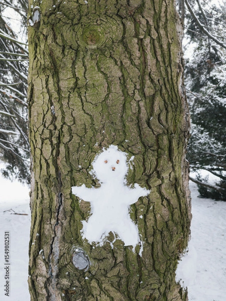 Fototapeta Snowman figure created on tree bark, surrounded by snow in winter landscape
