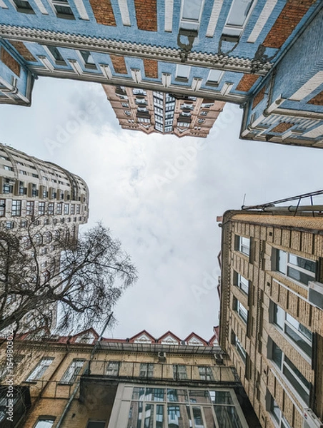 Fototapeta Upward view of buildings with cloudy sky. Urban architecture perspective showcasing modern and classic structures