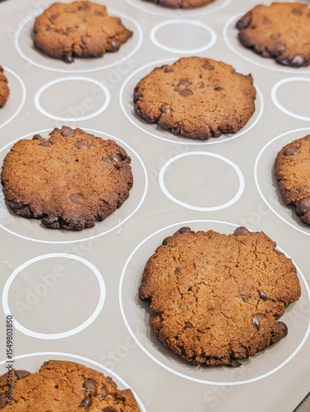 Fototapeta Baked chocolate chip cookies cooling on baking sheet lined with silicone mat