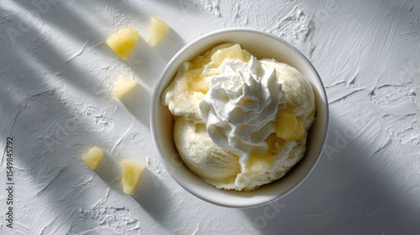 Fototapeta Refreshing dessert: Vanilla ice cream in a bowl topped with whipped cream and pineapple chunks.