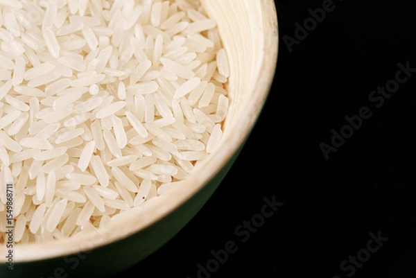 Fototapeta White rice grains in ceramic bowl on black background. Raw uncooked food in minimal style. Healthy carbohydrate source. Ingredient for cooking, diet, vegan or Asian cuisine.
