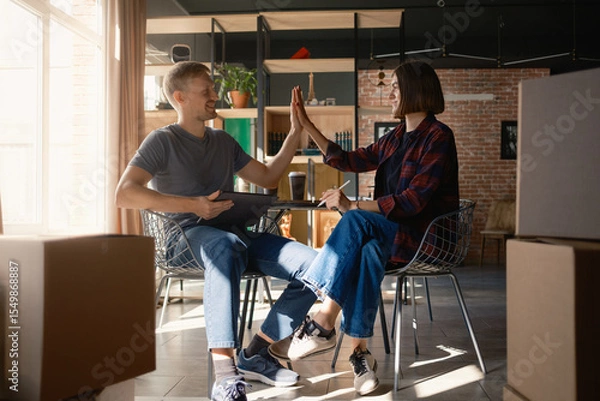 Obraz Smiling colleagues giving a high five while brainstorming ideas in a modern workspace