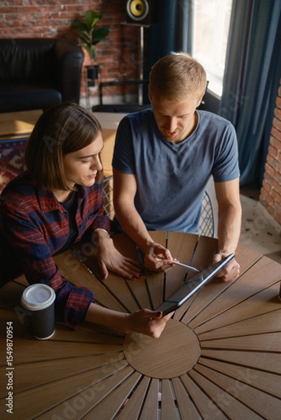 Obraz Two people work together at a circular table inside a warmly lit interior space.