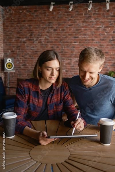 Obraz Two individuals collaborate on a tablet, enjoying a creative session with coffee