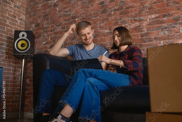 Obraz A couple sitting comfortably on a sofa, sharing an enjoyable moment together