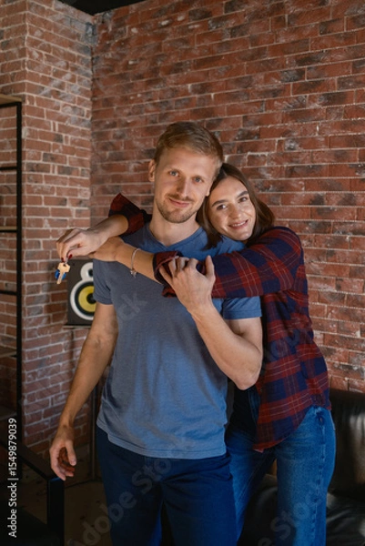 Obraz Smiling young couple showing a key while standing together in a modern interior