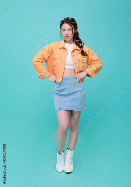 Fototapeta Portrait of an upset unsatisfied asian woman standing with hands on hips against isolated on blue background. Expresses annoyance displeasure.