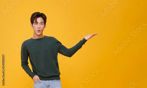 Fototapeta handsome asian man wow open mouth pointing finger to present something his hand gesture are perfect for the suggestion isolated on yellow copy space background.