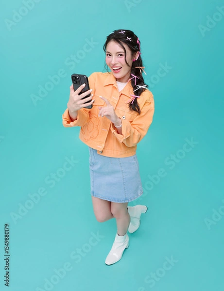 Fototapeta Top view Happy smiling young asian woman using mobile phone isolated on blue background. teen social media communication online.