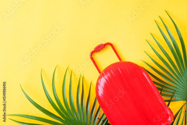 Fototapeta Red suitcase and palm leaves the yellow background. Travel and summer vacations concept. Mockup with copy space. Flat lay