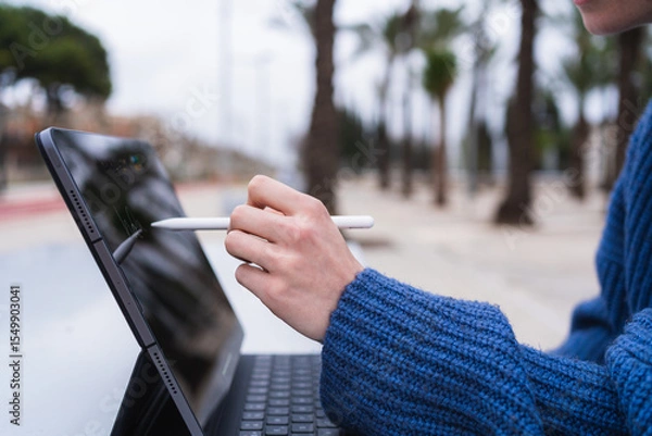 Fototapeta Student using tablet and stylus for online education in a park