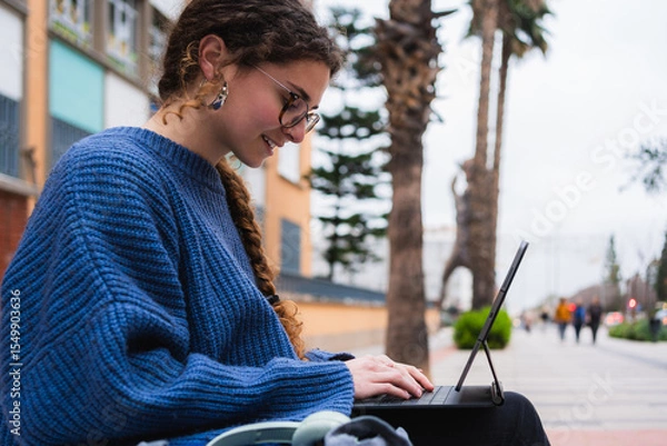 Fototapeta Young woman using tablet with keyboard, sitting on bench on university campus, studying outdoors