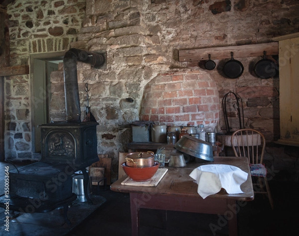 Obraz Authentic 19th-century rustic kitchen with a wood-burning stove, brick oven, and vintage cookware. Captures pioneer lifestyle and traditional cooking atmosphere in a historic Canadian setting.
