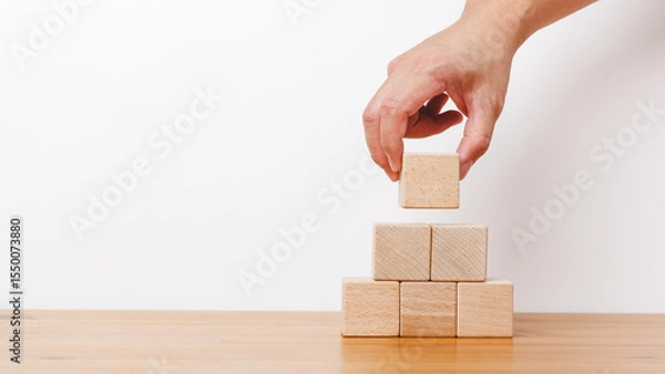Obraz Man hand holding empty wooden blocks and stack up in white background. Arranging of cube shape toy blocks in business concept on building, progress or development.