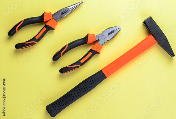 Fototapeta Hand tools including hammer and pliers on vibrant yellow background for repair concept