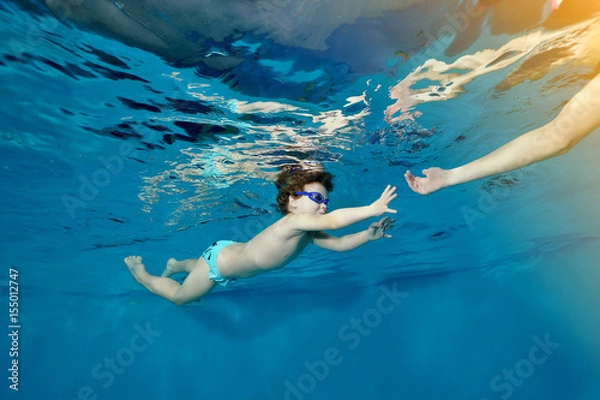Obraz Little girl swims underwater in the pool and reaches for the hand of the mother. Portrait. Bottom view from under the water. The landscape orientation