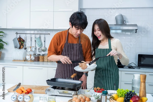 Obraz Happy portrait of loving young asian of having fun standing a cheerful preparing food and enjoy cook cooking with vegetables, meat, bread while standing on a kitchen Condo life or home